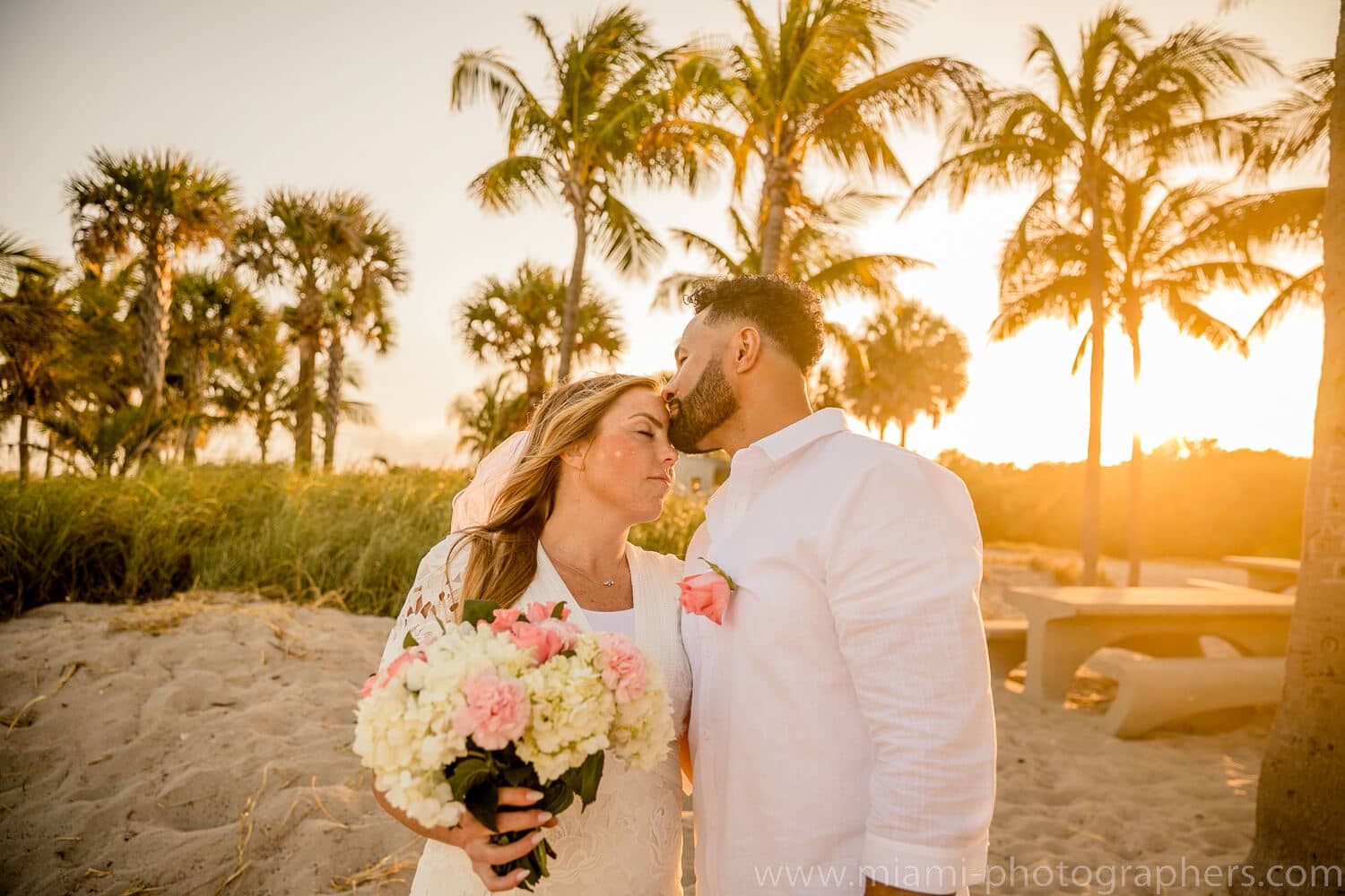 Bride and groom embracing at sunset during their intimate Miami beach wedding, with warm golden light and calm ocean waves in the background.