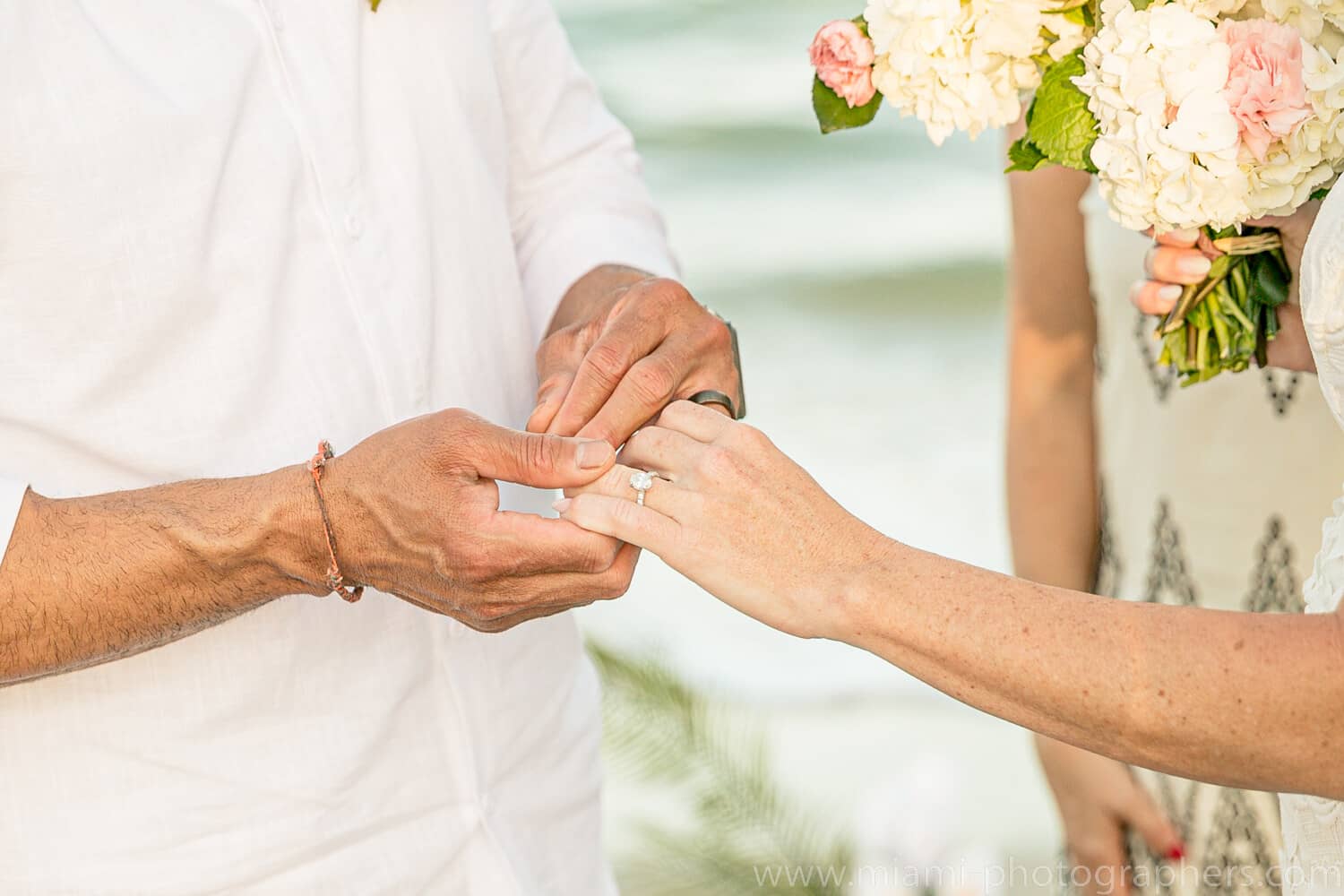 Bride and groom standing together on a sandy Miami beach during their intimate wedding, with ocean waves and soft natural light in the background.