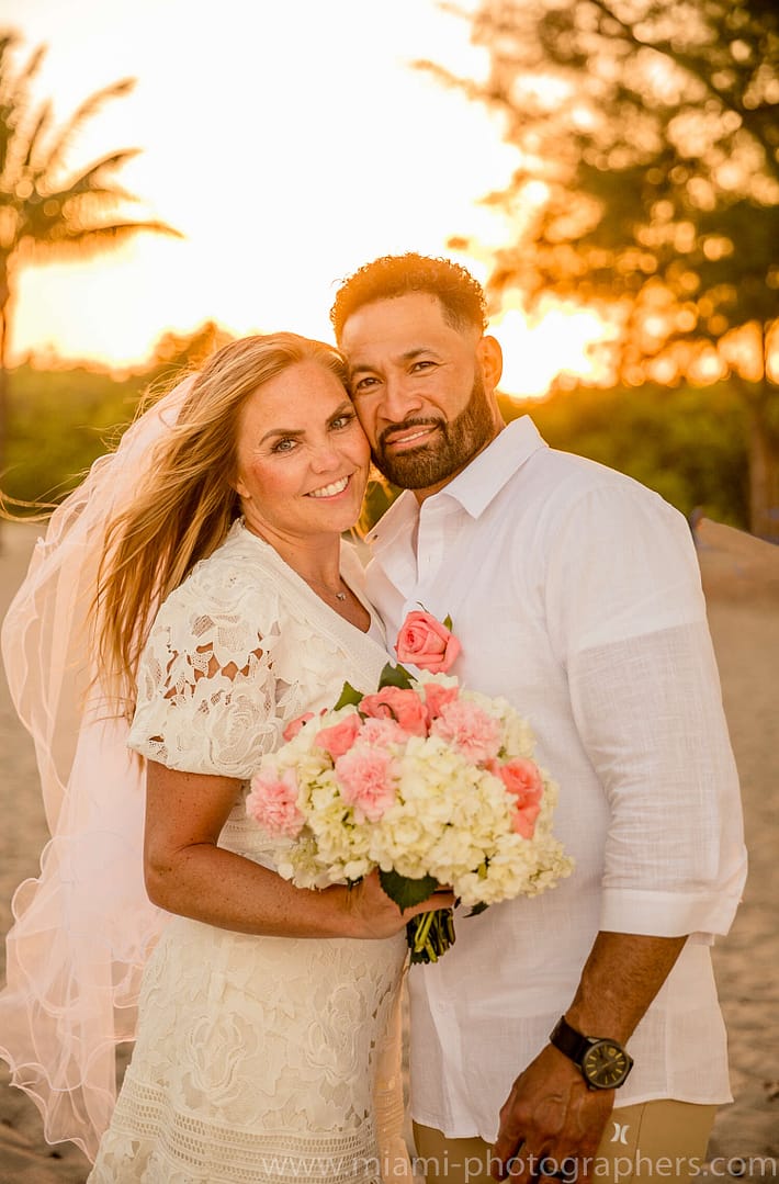 Bride and groom embracing at sunset on a Miami beach, with golden light reflecting off the ocean during their intimate wedding ceremony.