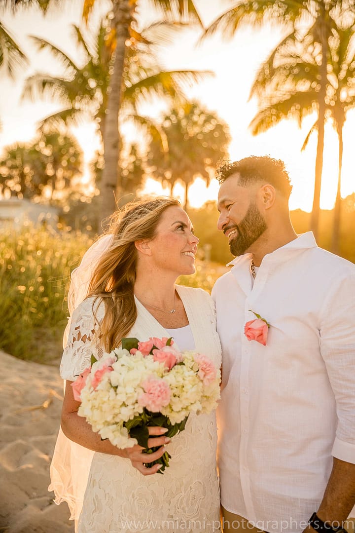 Bride and groom sharing a loving embrace at sunset during their Miami beach wedding, with soft golden light and the ocean as a backdrop.