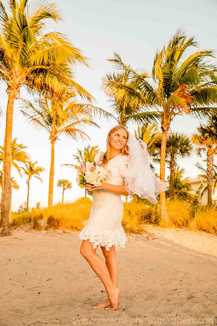 Bride and groom walking hand in hand along a Miami beach during their intimate wedding, with soft sunlight and gentle ocean waves.