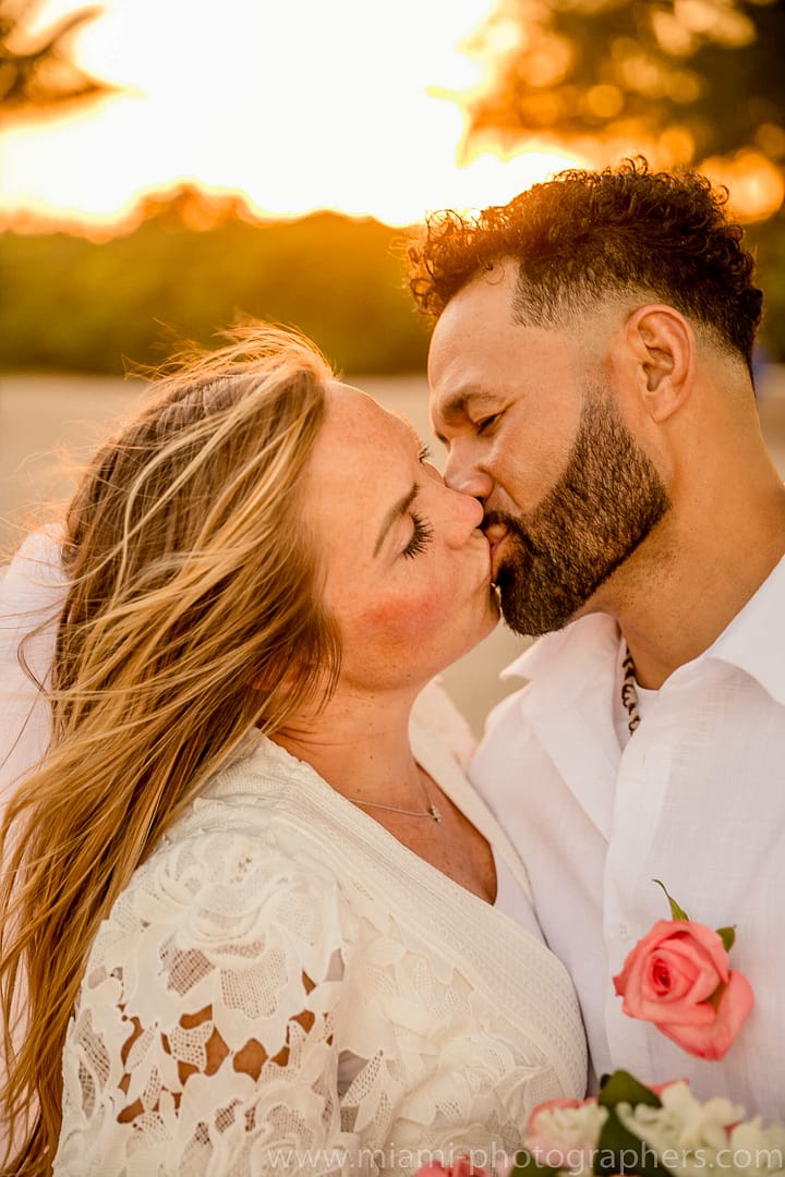 Bride and groom sharing a joyful moment on the sandy Miami beach during their intimate wedding, with soft natural light and ocean waves in the background.